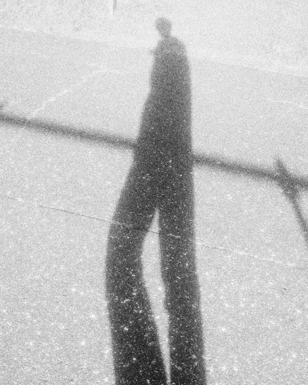 A long shadow of a person stretched across a road, light all around it
